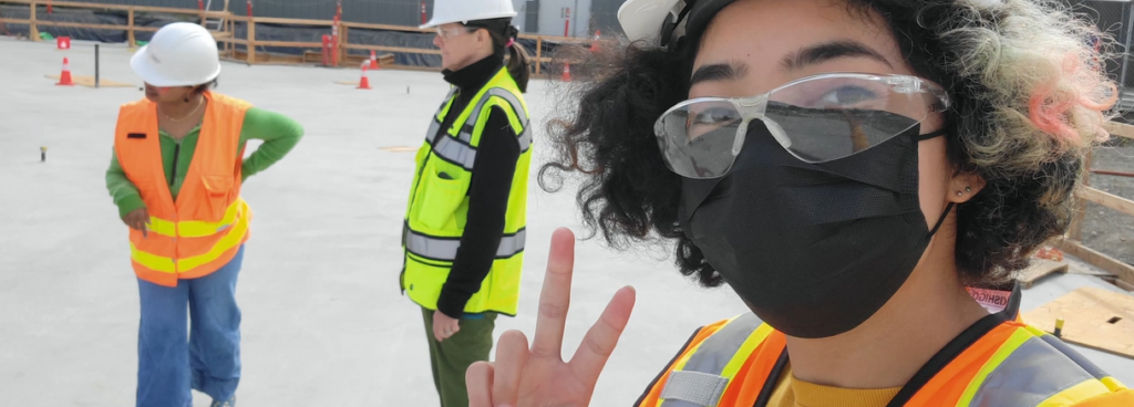 Student wearing mask holding up peace sign on construction job site